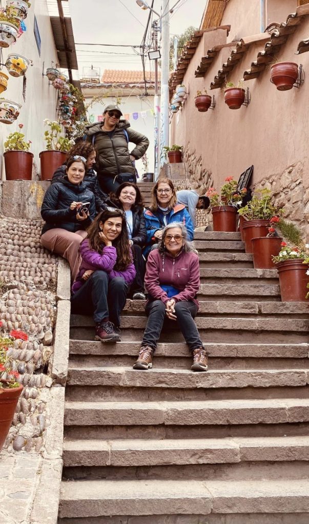 Grupo de mujeres sentadas en una escalera de piedra de una calle con macetas