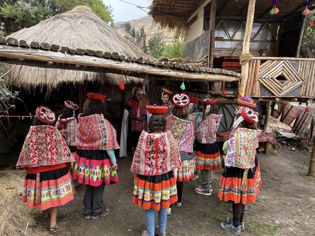 Mujeres andinas con coloridos trajes tradicionales en un patio frente a casas de techo de paja