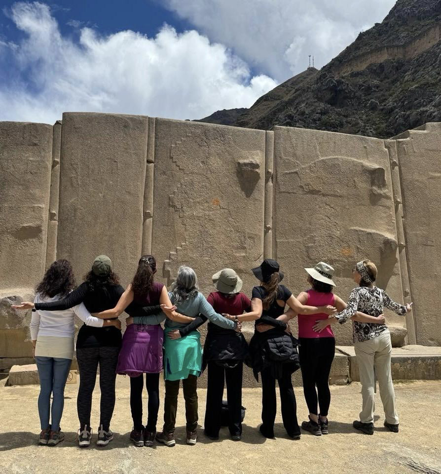 Grupo de mujeres abrazadas de espaldas frente a un gran muro de piedra inca
