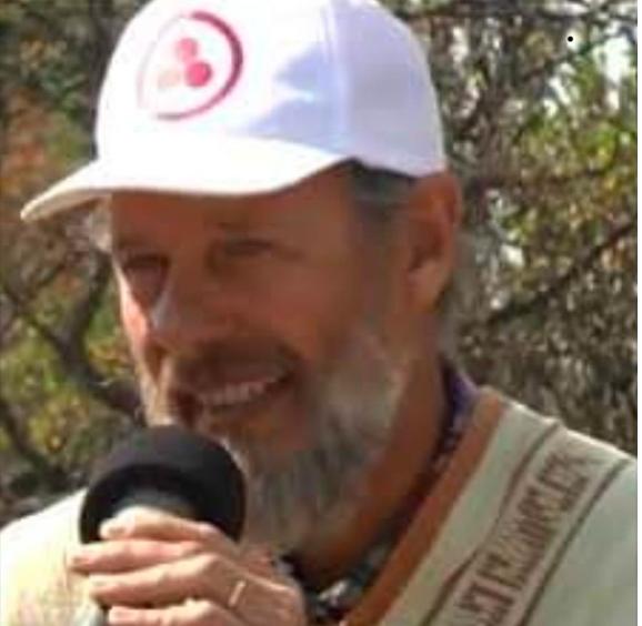 Oscar Acoglanis con gorra blanca hablando por un micrófono