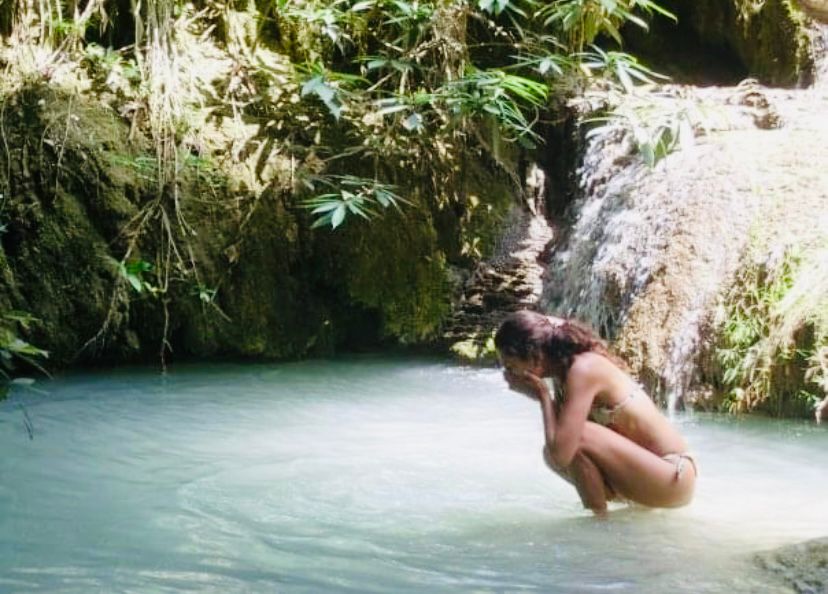 Mujer agachada en una poza de agua turquesa junto a una cascada, en Taman Negara, Malasia
