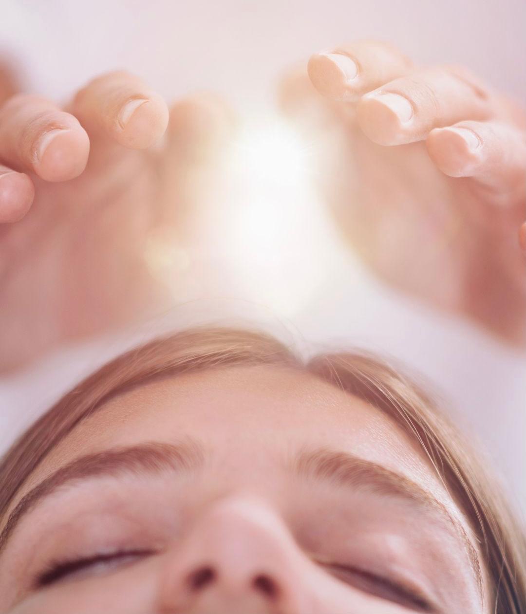 Manos sobre la frente de una persona con los ojos cerrados durante una sesión de Reiki