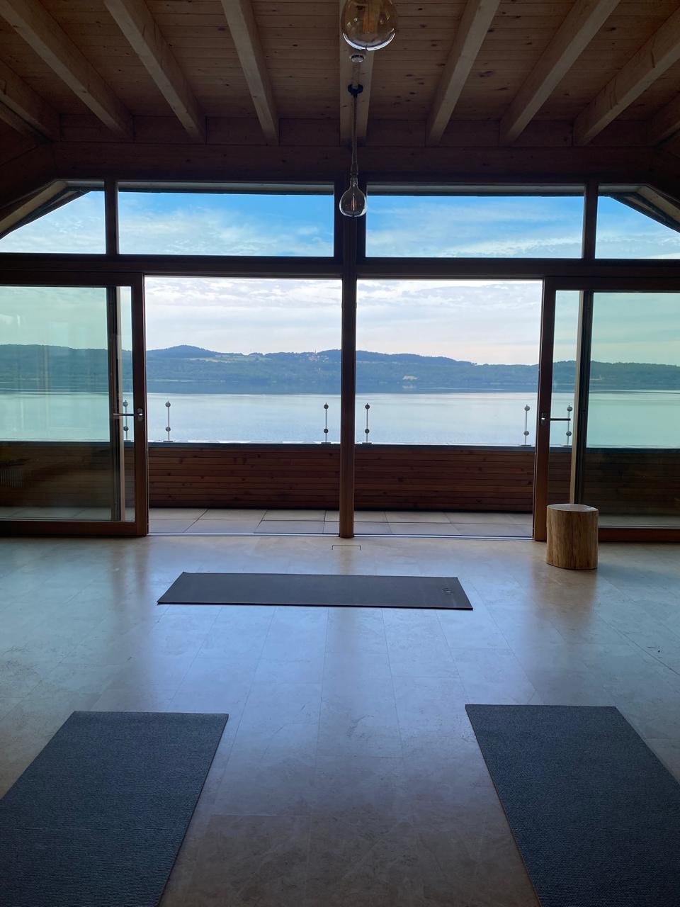 Sala de yoga con esterillas y grandes ventanales con vista a un lago
