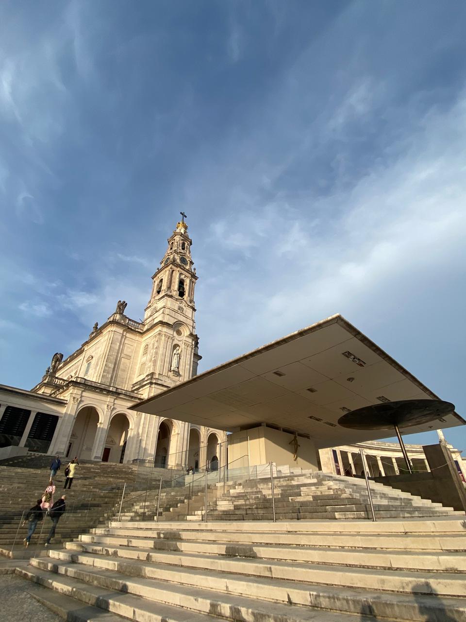 Basílica del santuario de Fátima con su torre y una gran escalinata bajo un cielo con nubes