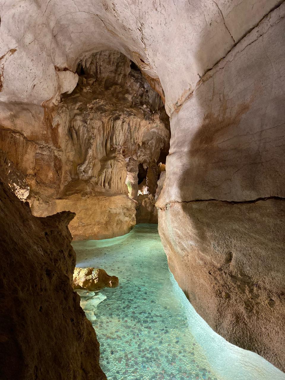 Cueva con formaciones de roca y un estanque de agua turquesa con monedas en el fondo