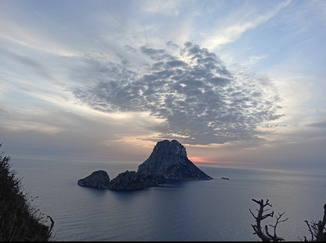 Es Vedrá al atardecer: islote rocoso en el mar bajo un cielo con nubes